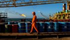 A worker passes stores of oil drums and gas flares while working aboard an offshore oil platform. Photographer: Ali Mohammadi/Bloomberg
