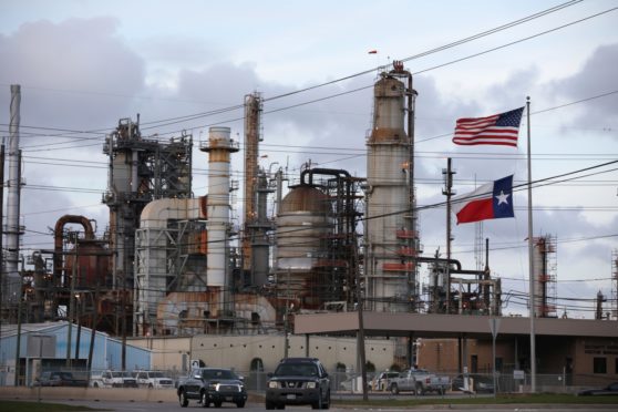 An American and Texas flag stand in front of the Chevron Corp. Pasadena Refinery in Pasadena, Texas, U.S., on Sunday, March 8, 2020. Houston has been purposefully going green for more than a decade. The municipal government gets 92% of all the power it uses in the buildings it owns from wind and solar and has been on the U.S. Environmental Protection Agency's list of the largest renewable power users since 2016. Photographer: Sharon Steinmann/Bloomberg