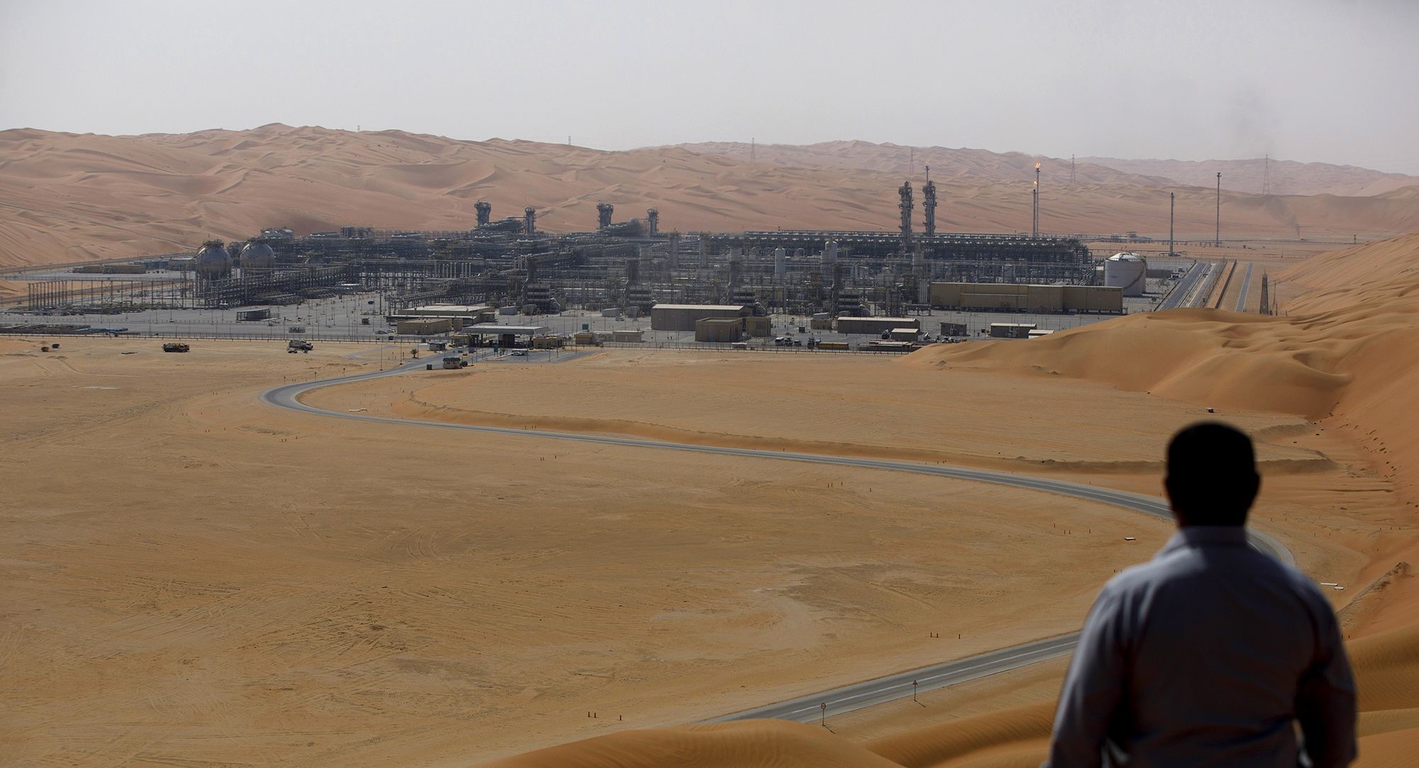 Worker in bottom right hand corner looks over desert to industrial facility