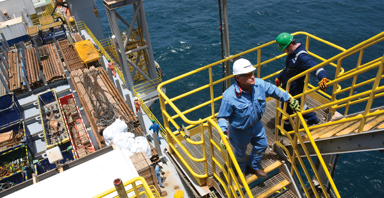 Man in hard hat walks up yellow stair way offshore