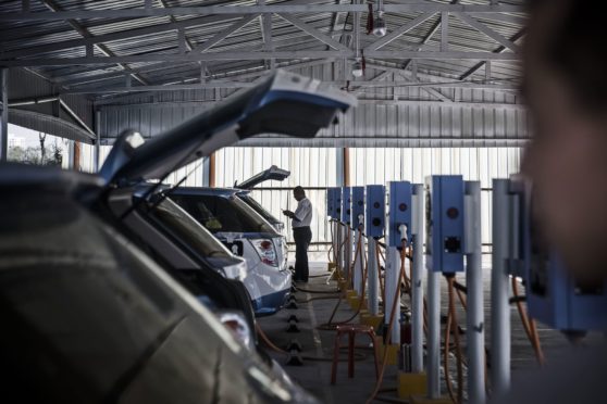 A driver uses a smartphone in front of BYD Co. E6 electric taxis while they charge at a charging station in Taiyuan, Shanxi province, China, on Tuesday, Sept. 13, 2016.