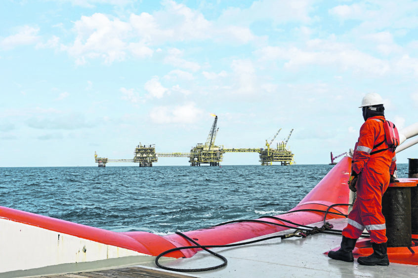 Marine crew complete wearing Personal Protective Equipment (PPE) standing near to shark jaws at stern vessel while looking through to the oil and gas platform in the middle of the sea.