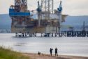 Pedestrians walk along a beach near the Noble Sam Turner jack-up drilling rig, operated by Noble Corp., in Cromarty, U.K. Photographer: Jason Alden/Bloomberg