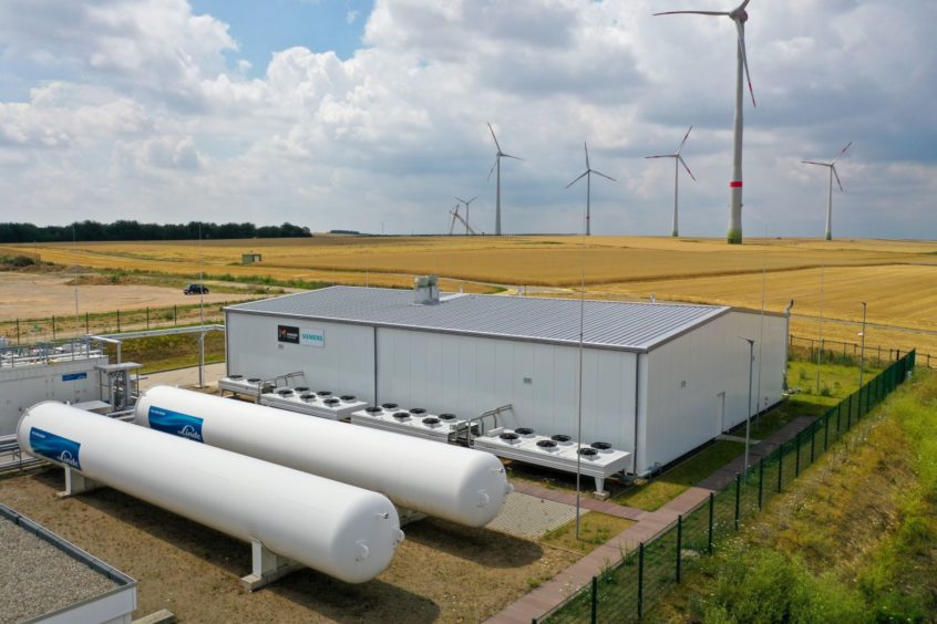 Wind turbines stand in view of the hydrogen electrolysis plant stands.