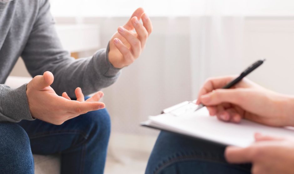 Psychotherapist writing notes, assessing patient's health and giving diagnosis to man sitting on couch during counseling session , panorama, free space; Shutterstock ID 1374539876; Purchase Order: EV supplement; Job: Int SOS column; 905f4169-aad3-422f-85c1-8627d4105cfc