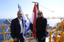 Two men stand next to flags with sea behind them