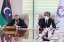 Two men sit at meeting table with Libyan flag