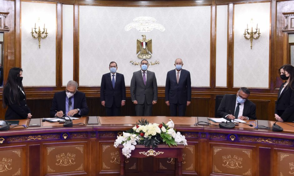 Three men in suits watch two men in suits sign deal