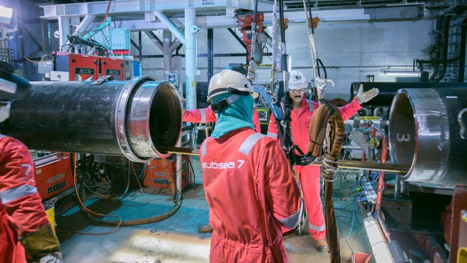 Men in overalls move pipeline sections onboard a ship