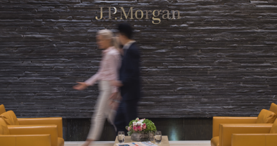 Two blurry people walk in front of wall saying JP Morgan