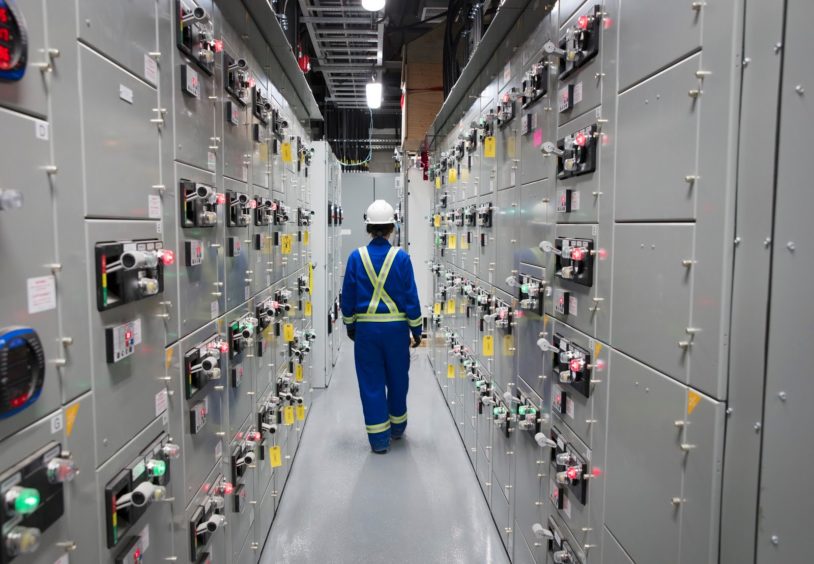 Worker in blue overalls walks away between electrical equipment