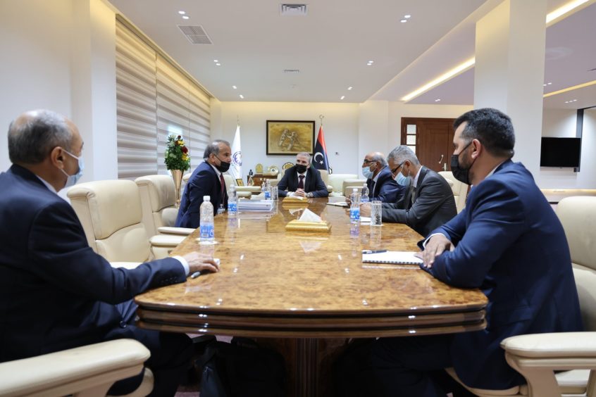 Men sit at conference table in cream seats.