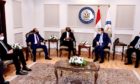 A group of men sit in chairs talking, beneath an Egyptian flag