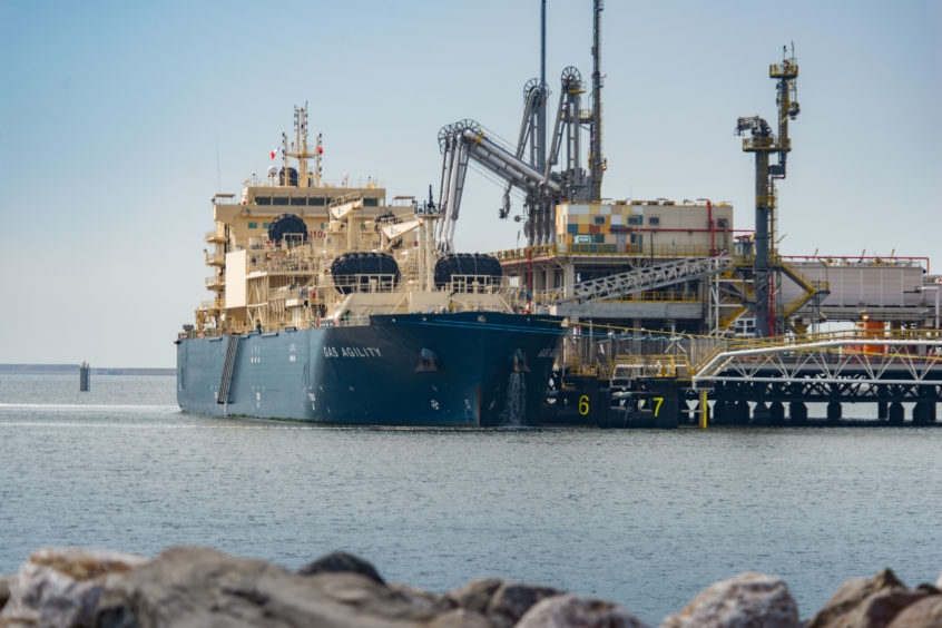 An LNG bunker vessel docked at a jetty, with rocks in foreground