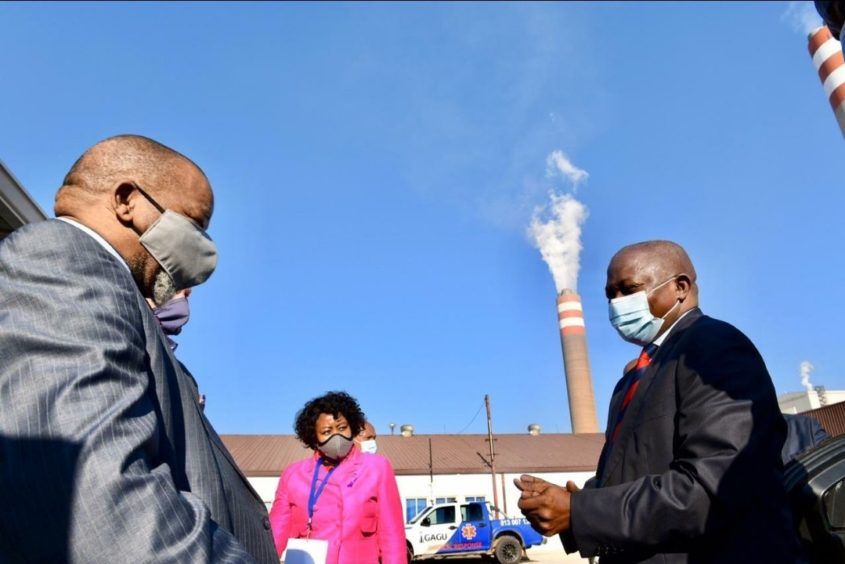 Two men in suits meet with a chimney in the background