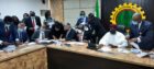 Men in suits sit at a table signing documents, with NNPC logo behind