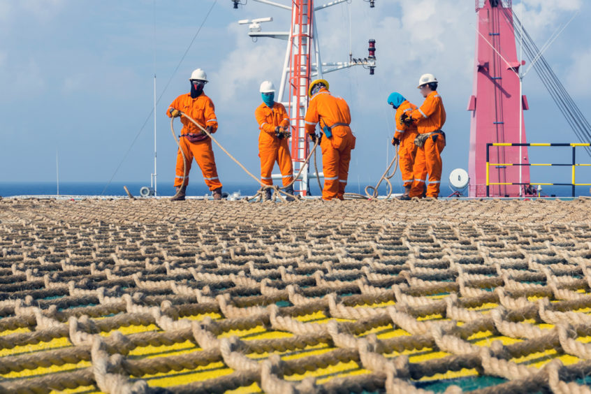 A group of overall-clad workers on a deck, covered with a net