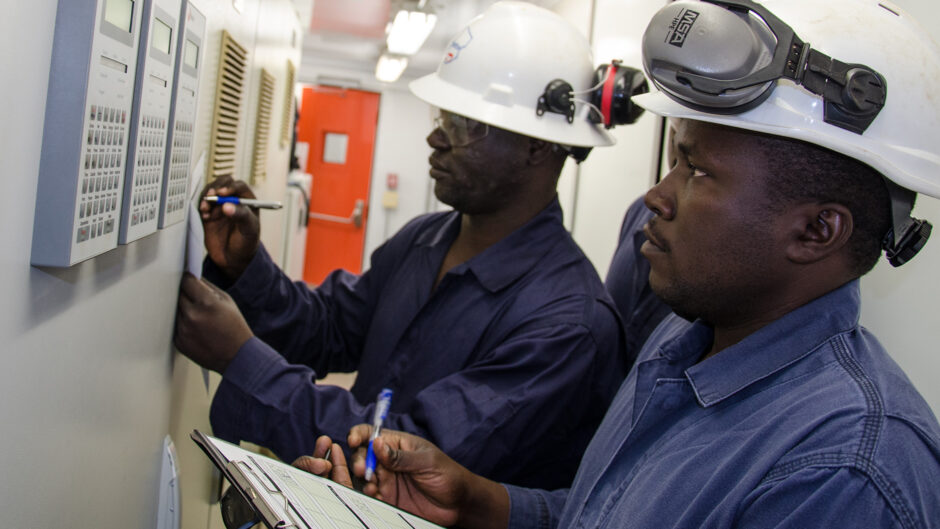 Two workers in hard hats check instruments