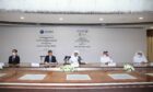 Five men sit at a big table signing deal documents