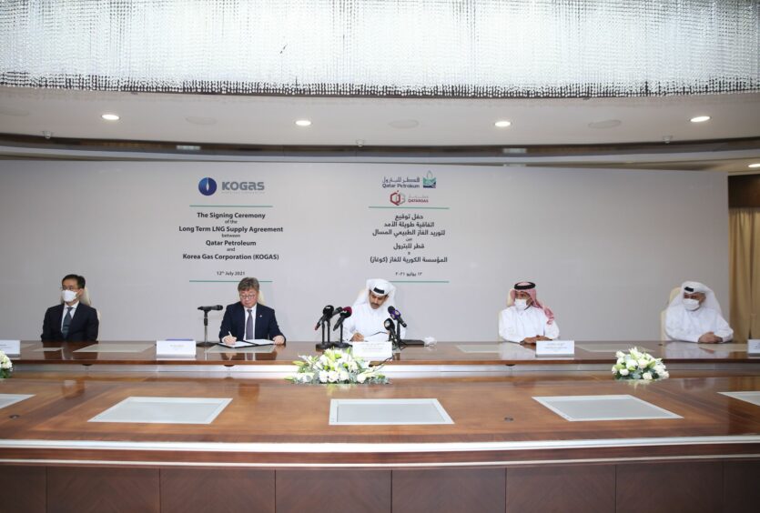 Five men sit at a big table signing deal documents