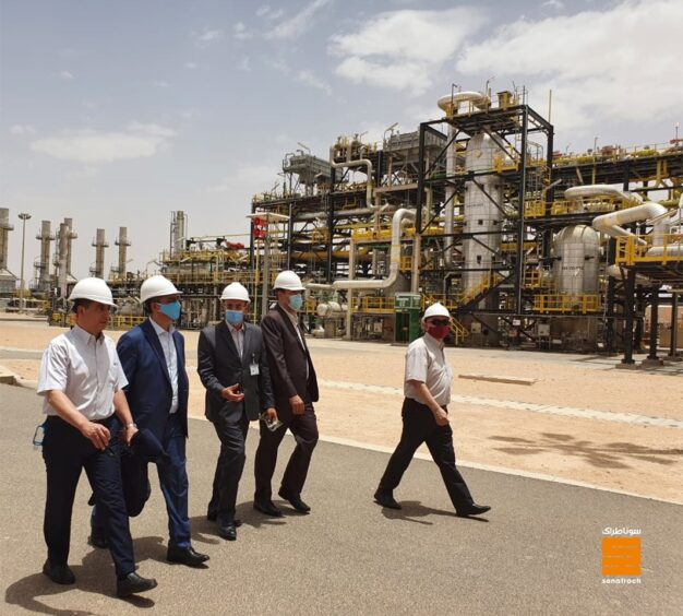 Men in hard hats walk past industrial machinery