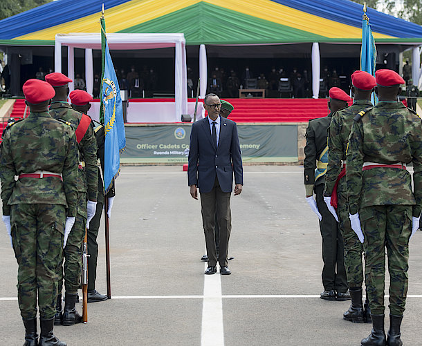 Man in suit stands between soldiers in red berets