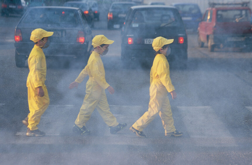 Three children in yellow overalls cross a cloudy road