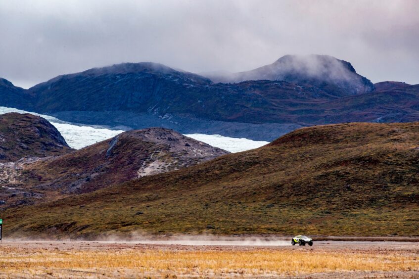 SUV races across big landscape with mountains and clouds behind