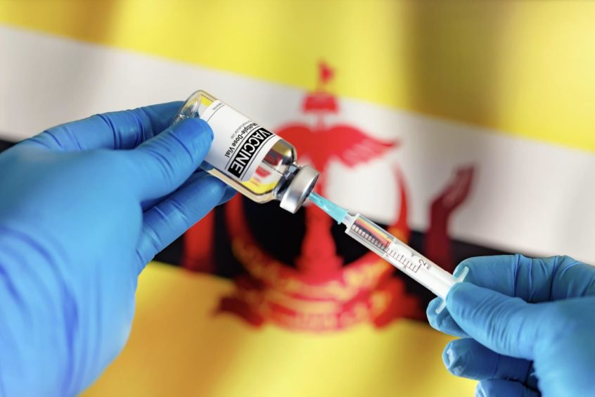 Doctor preparing vial of vaccine injection for the vaccination plan against diseases in Brunei against the country's flag.