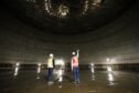 Two men stand inside massive tank pointing upwards
