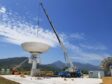 A crane lowers a satellite dish against a blue sky
