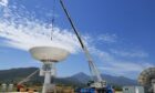 A crane lowers a satellite dish against a blue sky