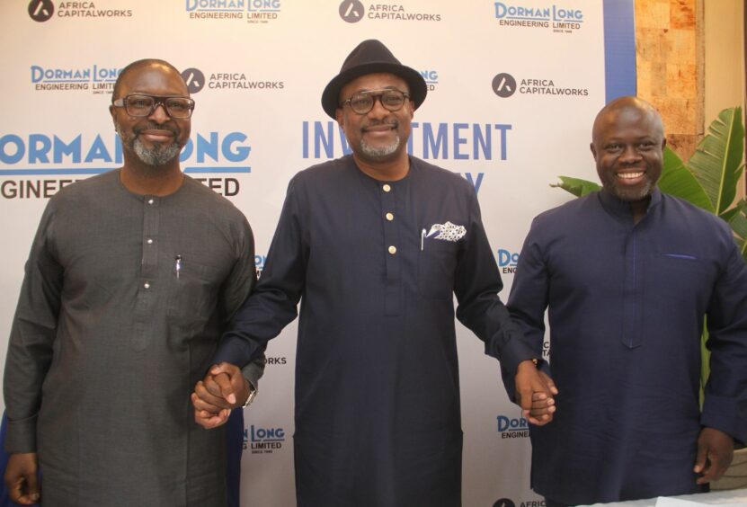 Three men hold hands in front of a backdrop with logos