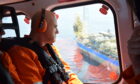 Man in headphones looks out of helicopter at big ship