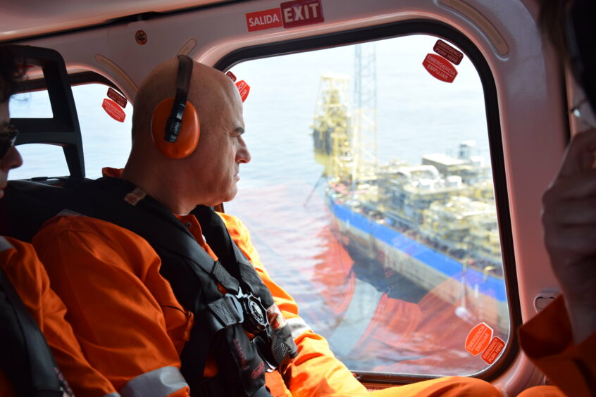 Man in headphones looks out of helicopter at big ship