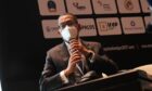 Man in a mask speaks into a mic in front of company logos