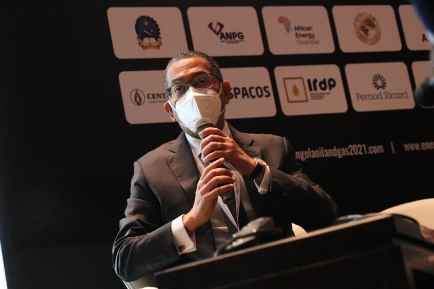 Man in a mask speaks into a mic in front of company logos