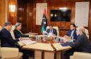 Men sit round a table in front of Libyan flag