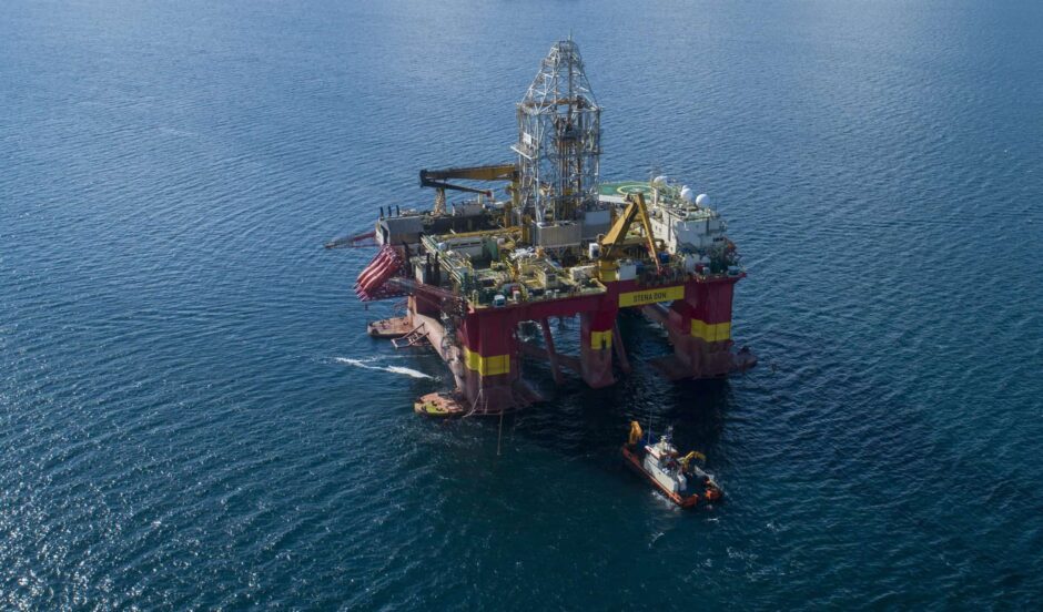 A drilling rig in a deep blue sea with a smaller vessel in front