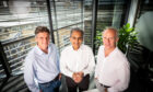 Three men in shirts look at camera, with open blinds behind