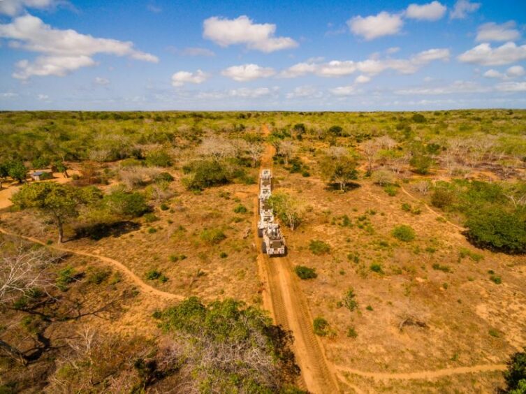 Seismic trucks drive across an orange landscape with scrubby brush