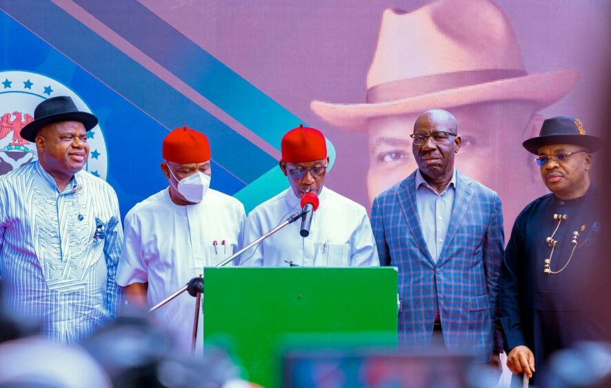 Men stand at a podium, one with a red hat speaks into a mic