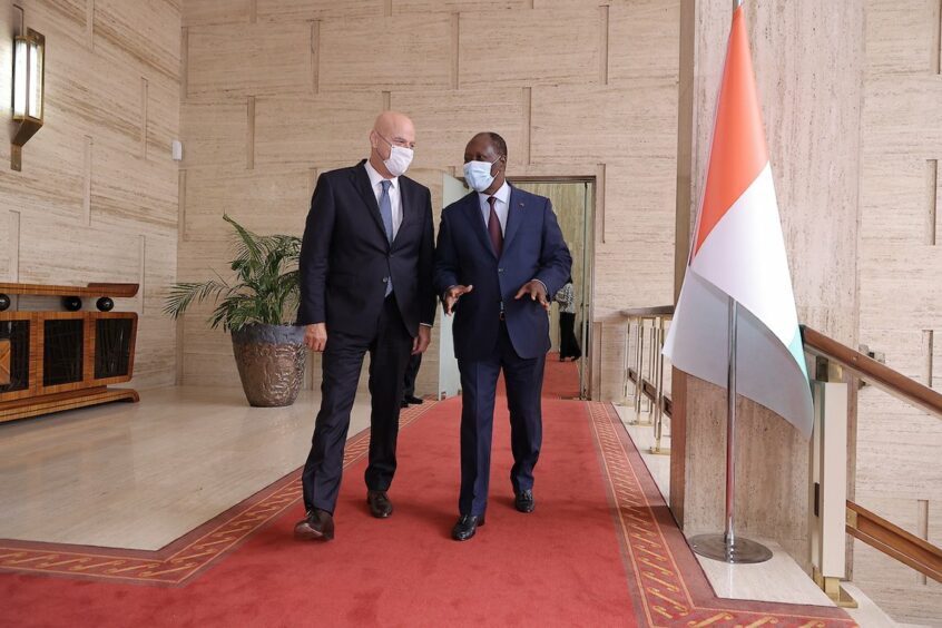 Two men walk along talking while wearing masks on a red carpet