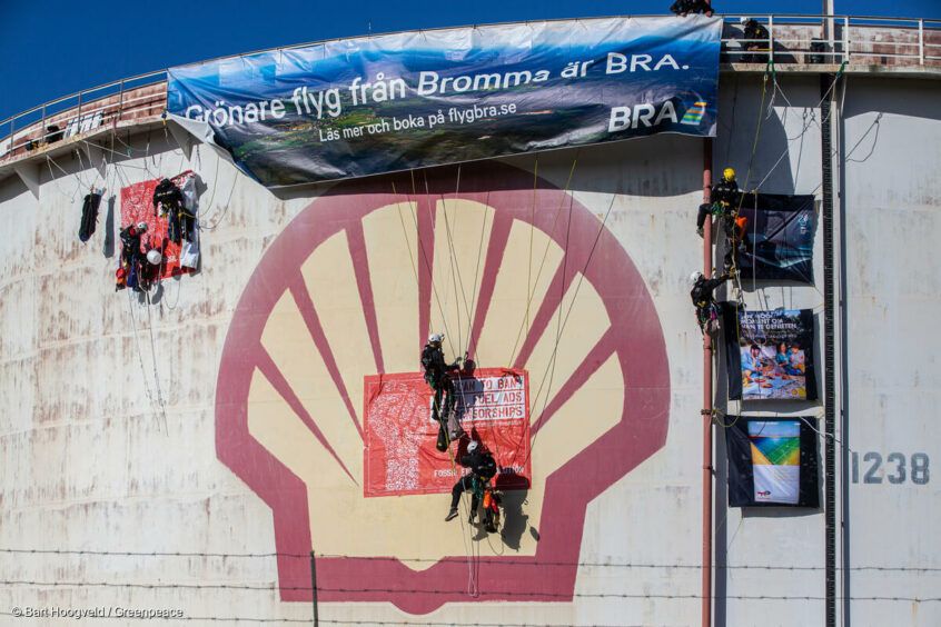 Climbers attach a banner to the top of an oil tank over a Shell logo