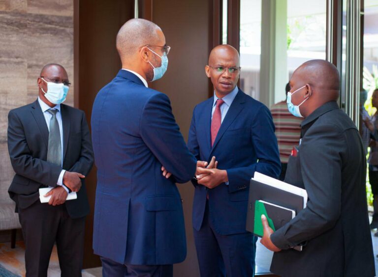 Men in suits talk next to a window