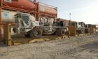 A big truck on a loader in front of some tanks