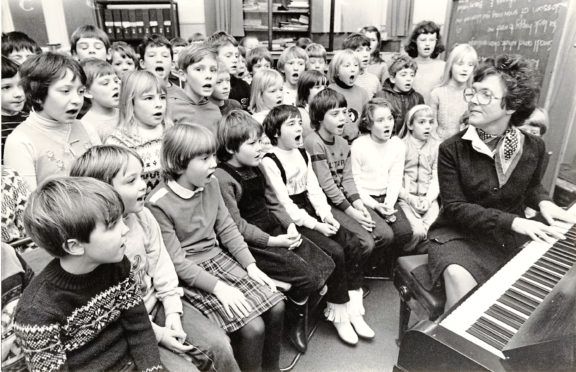 Music teacher Anne Garden accompanies a choir in 1982