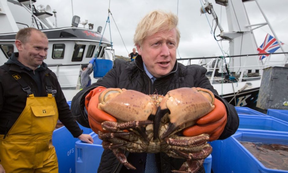 Prime Minister Boris Johnson holds crabs caught on the Carvela with Karl Adamson at Stromness Harbour during a visit on July 23 2020.
