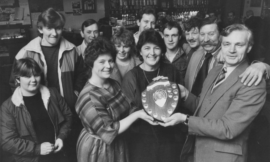 The Lord Byron Bar at Northfield won the Royal National Institute for the Blind competition for the biggest pile of pennies to be collected for institute funds in 1984. Bar staff Norah Gribble and Georgie Boyle were presented with the Andy Stewart Shield watched by bar manager Sandy Cruickshank and customers.