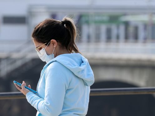 A woman wearing a mask looks at her phone under a sign saying ‘Stay Home’ projected from Bournemouth pier, as the UK continues in lockdown to help curb the spread of the coronavirus.